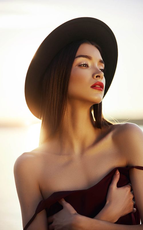 Portrait of a beautiful woman with long hair in a big round black hat. Beauty skin face, bare shoulders. Girl golden light at sunset
